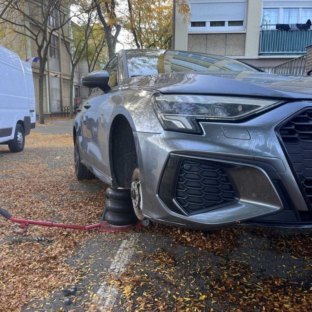Une Audi A3 grise est surélevée à l'aide d'un cric et de cales. Service par First Pneu.